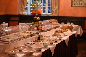 En buffé med ett varierat utbud av mat, inklusive frukt, sallader och bakverk, uppdukad på ett bord med utsikt över ett vackert dekorerat fönster i bakgrunden.
