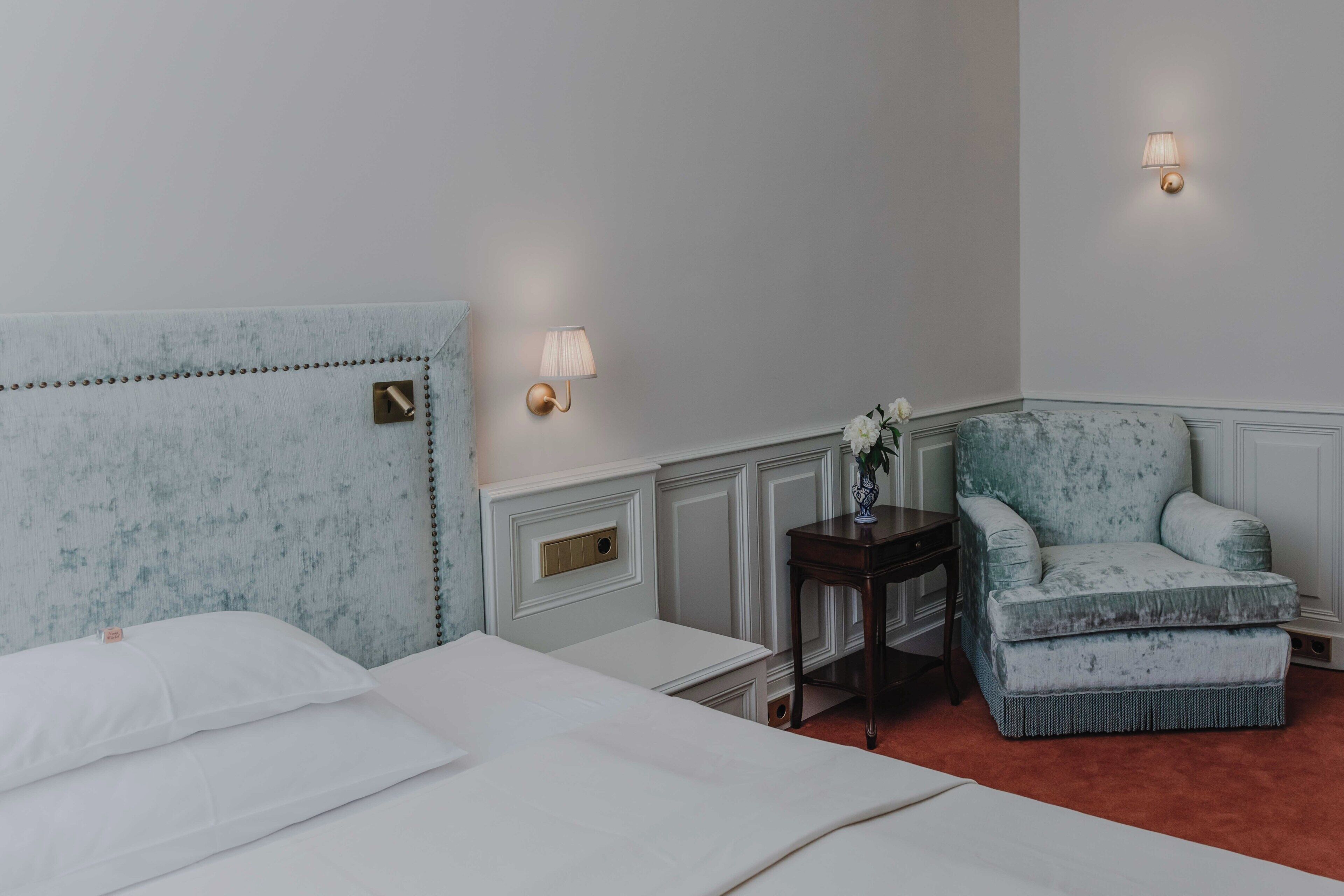Habitació d'hotel amb llit, una cadira, taula petita i dues làmpades fixades a la paret.