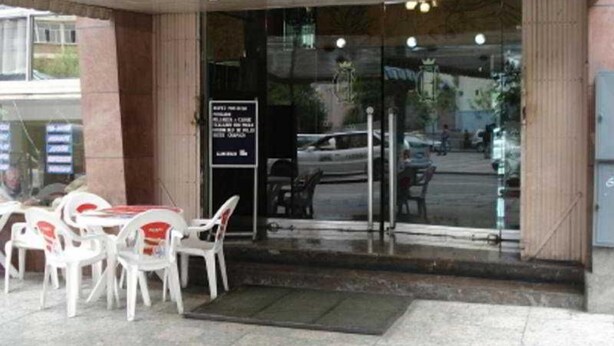 Entrada de un hotel con puerta de vidrio, cartel y mobiliario exterior con sillas.