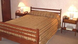 Habitación estándar de hotel con una cama individual, dos mesitas de noche con lámparas, un cuadro enmarcado en la pared y una puerta a la izquierda.
