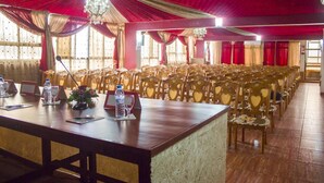 A banquet hall with rows of wooden chairs, a long table with nameplates and water bottles, and red drapes. - Atenas Hotel (Tetouan)