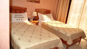 Dos camas dobles con cubrecamas estampados, una mesita de noche con lámpara y un cuadro en la pared.