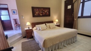 A neatly arranged bedroom with a large bed, two bedside tables with lamps, a framed picture on the wall, and a door with curtains.