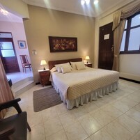 Un dormitorio ordenado con una cama grande, dos mesitas de noche con lámparas, un cuadro en la pared y una puerta con cortinas.