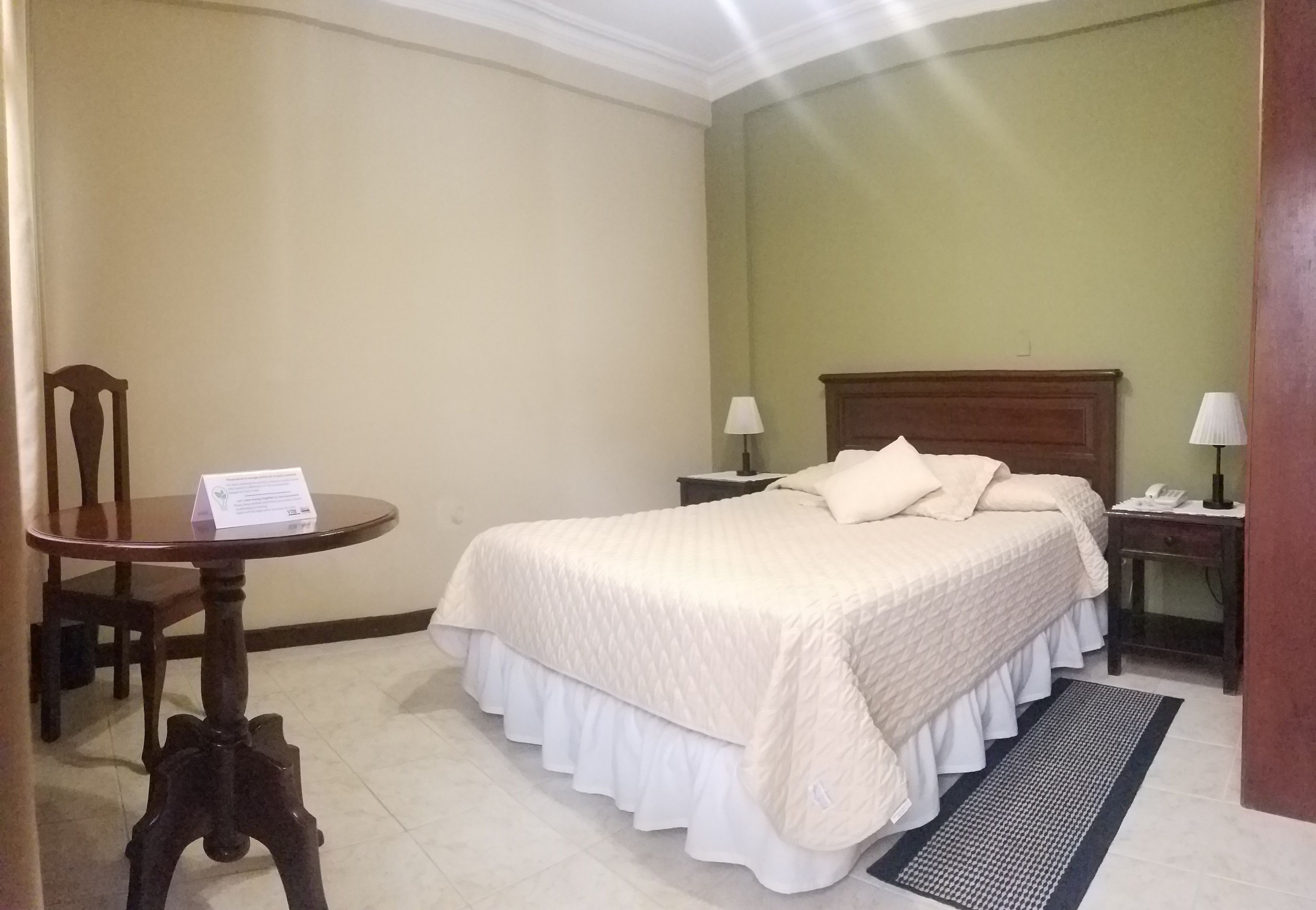 A hotel room with a bed, two bedside tables, a chair, and a small table with a sign.