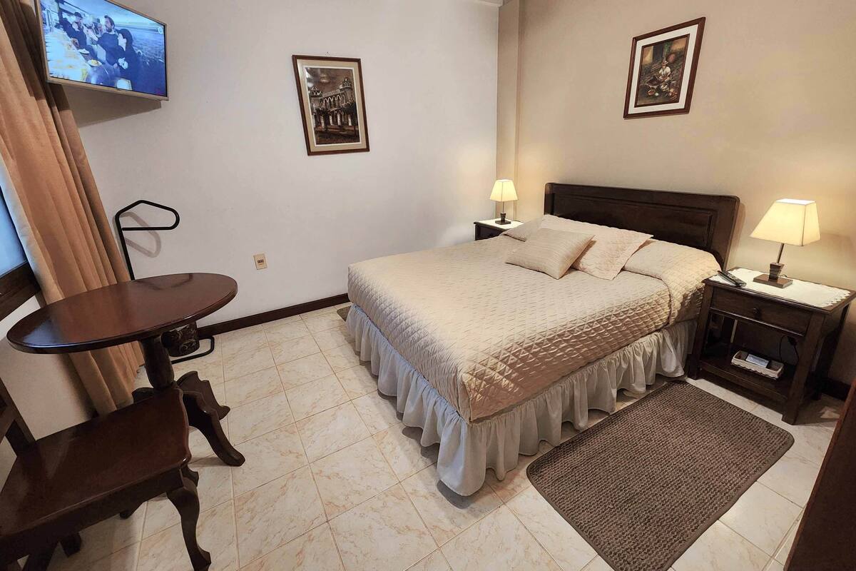 A hotel room with a bed, two bedside tables with lamps, a TV mounted on the wall, and two framed pictures on the wall.