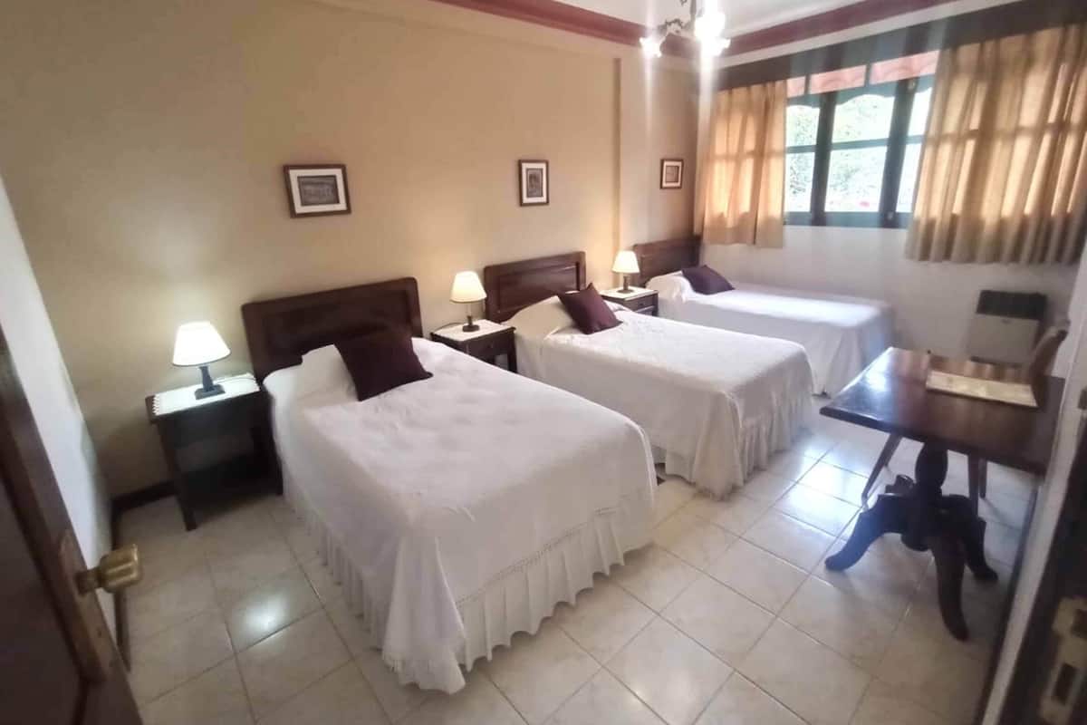 A hotel room with two single beds, a small table, and a chair.