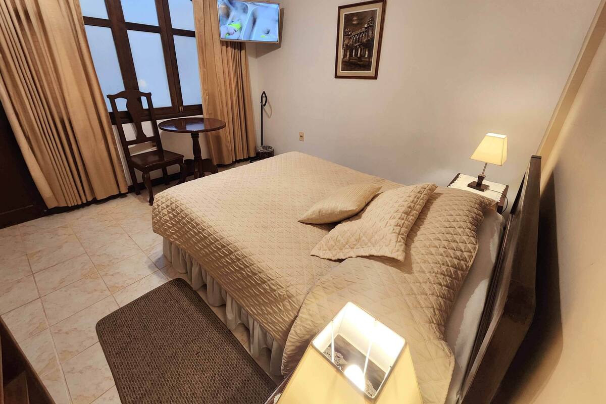 A hotel room with a bed, a TV mounted on the wall, a small table, and a chair.