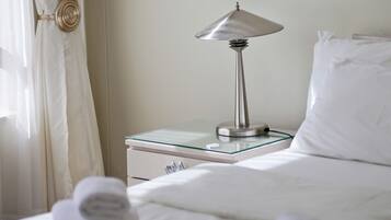 A neatly made bed with white linens, a glass-top bedside table with a metallic lamp, and a white pillow.
