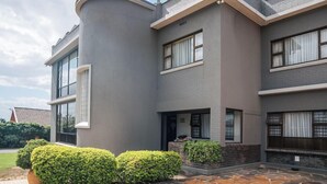 A modern two-story house with a curved corner, large windows, and a stone-tiled patio. - Harewood Lodge (East London)