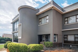 A modern two-story house with a curved corner, large windows, and a stone-tiled patio. - Harewood Lodge (East London)