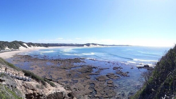 A coastal landscape with rocky terrain, a sandy beach, and a clear sky. - Harewood Lodge (East London)