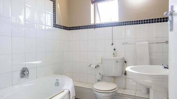 A bathroom with a bathtub, toilet, and sink, tiled walls, and a window.