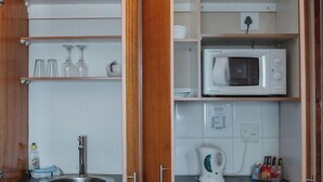 A compact kitchen with wooden cabinets, a built-in microwave, a kettle, and a sink. - Harewood Lodge (East London)