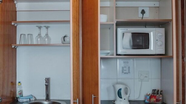 A compact kitchen with wooden cabinets, a built-in microwave, a kettle, and a sink. - Harewood Lodge (East London)