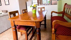 A dining area with a wooden table and chairs, a green vase with flowers, and a kitchen in the background. - Harewood Lodge (East London)