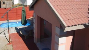 Un edificio residencial con piscina, cerca roja y sombrilla verde.