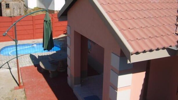 A residential building with a swimming pool, a red fence, and a green umbrella. - All Are Welcome (Brakpan)