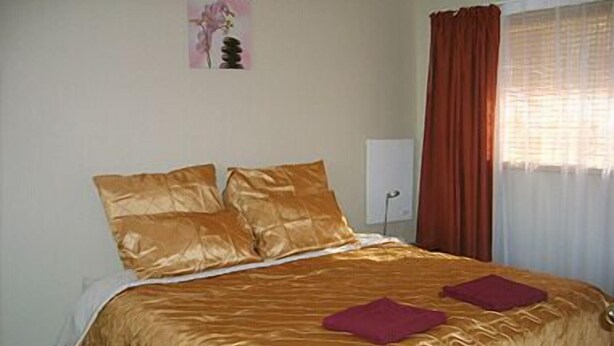 Una cama con cubre color dorado, dos almohadas y dos toallas rojas.