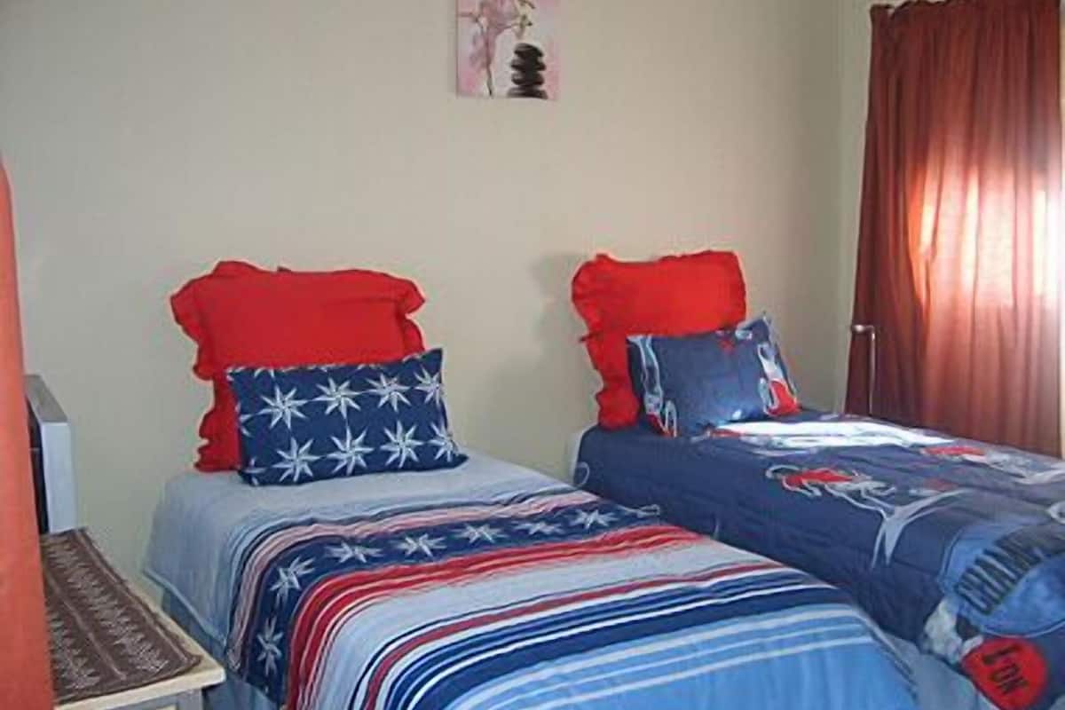 A bedroom with two beds, each with red and blue bedding, and a small table with a lamp.