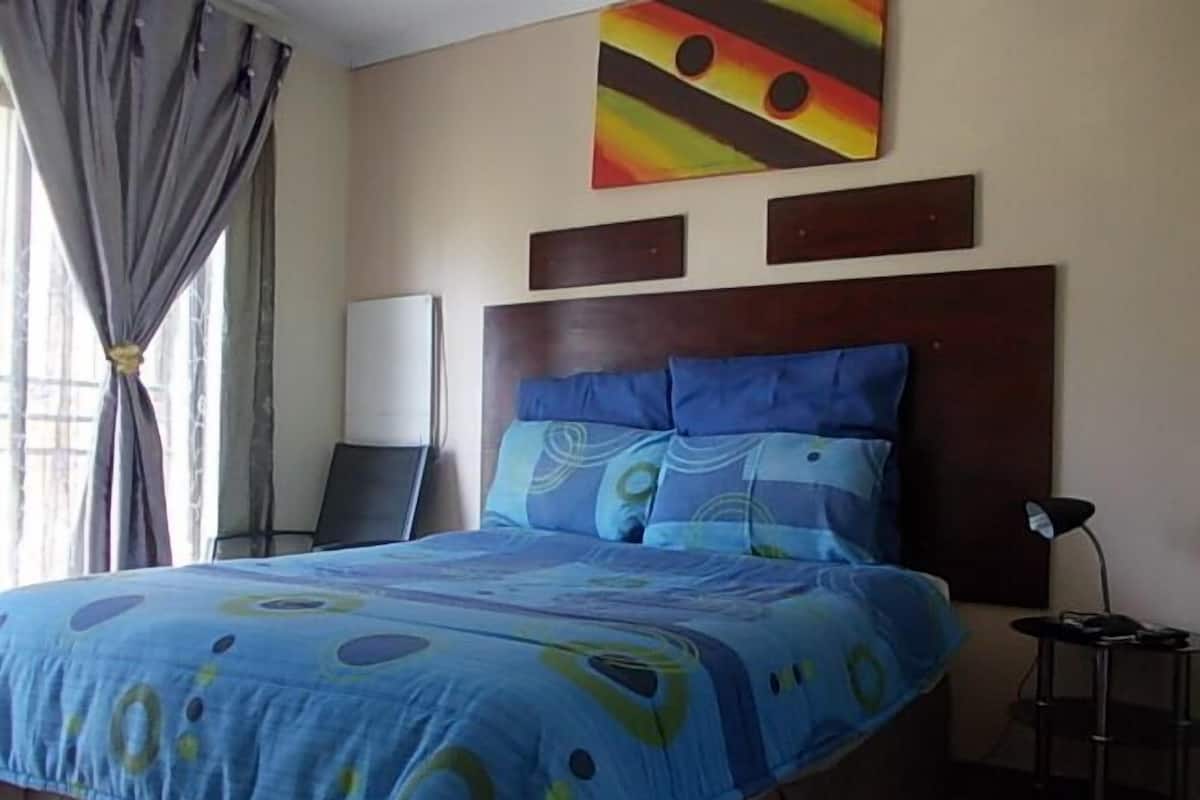 A hotel room with a bed, a nightstand, a lamp, and a painting on the wall.