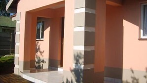 A building with a pink facade, a covered entrance, and a window. - All Are Welcome (Brakpan)