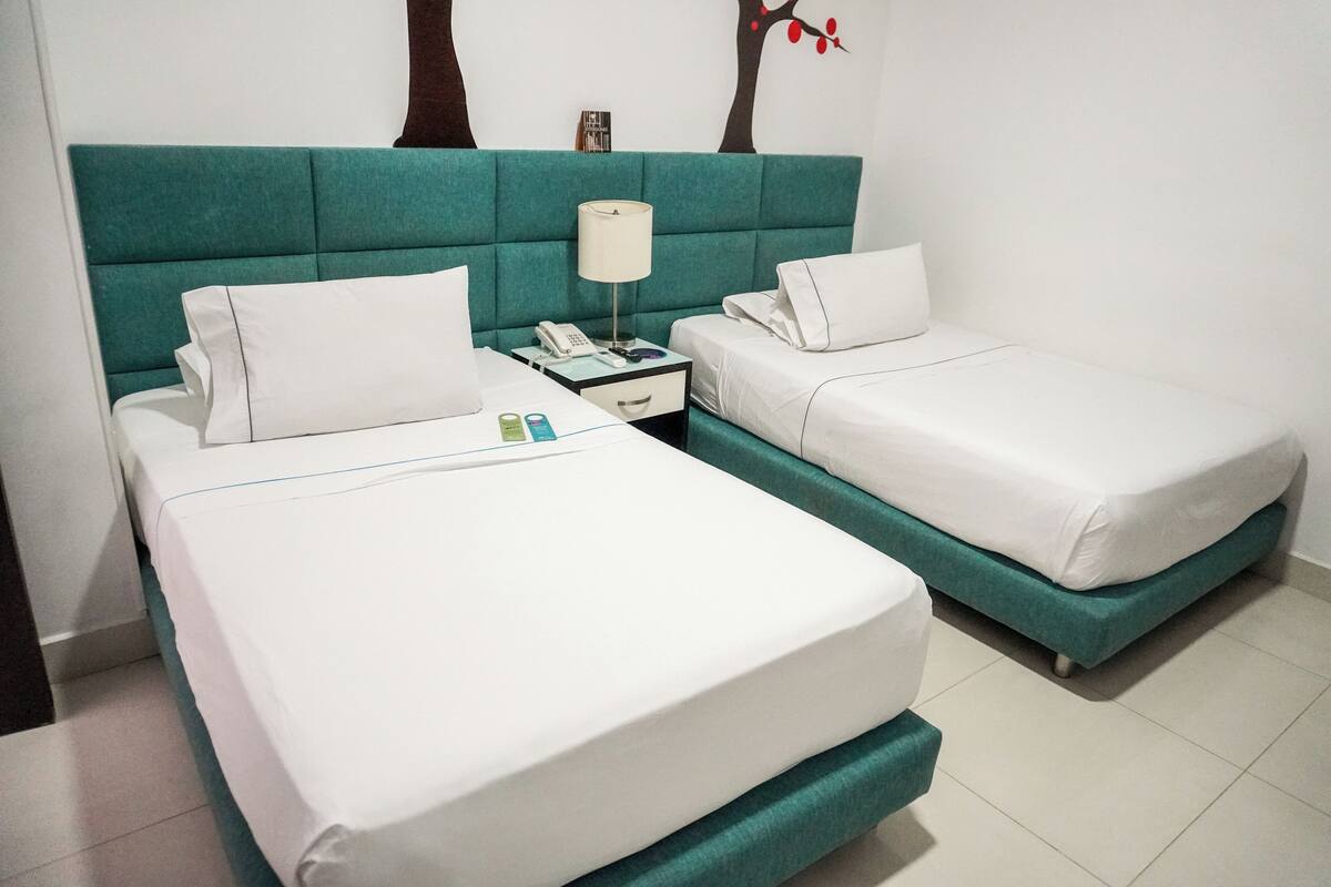 A hotel room with two beds, a nightstand with a phone and lamp, and a wall decoration.