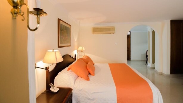 Ein Hotelzimmer mit Bett, Nachttisch mit Lampe, einem Bild an der Wand und einer Klimaanlage.