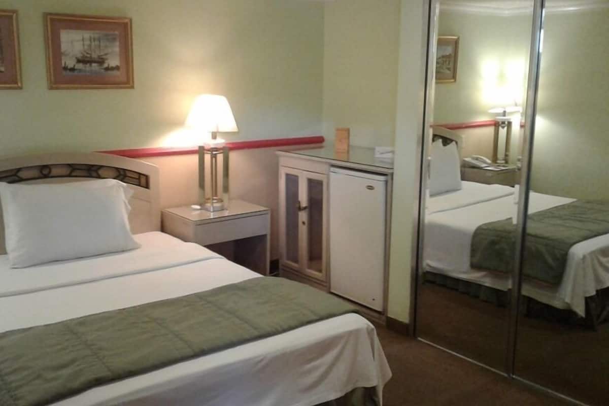 A hotel room with a bed, a nightstand with a lamp, a small cabinet, and a mirror.