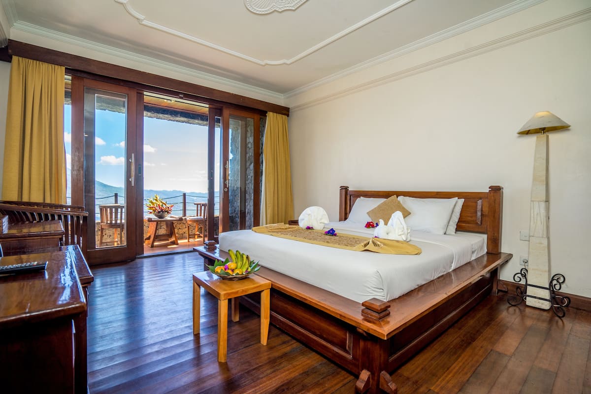A spacious bedroom with a large bed, wooden furniture, a piano, and a view of the outdoors.