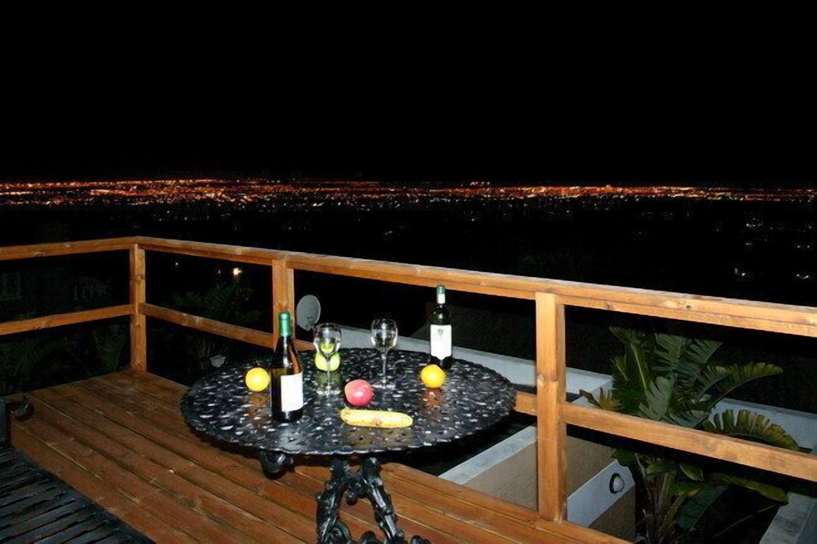 A wooden deck with a round table set for dining, featuring bottles and fruits.