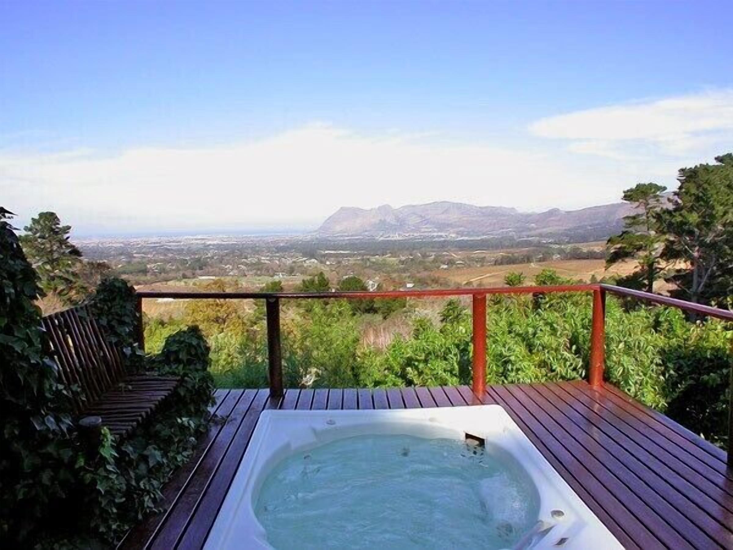 A hot tub on a wooden deck with a view of a city and mountains in the distance.