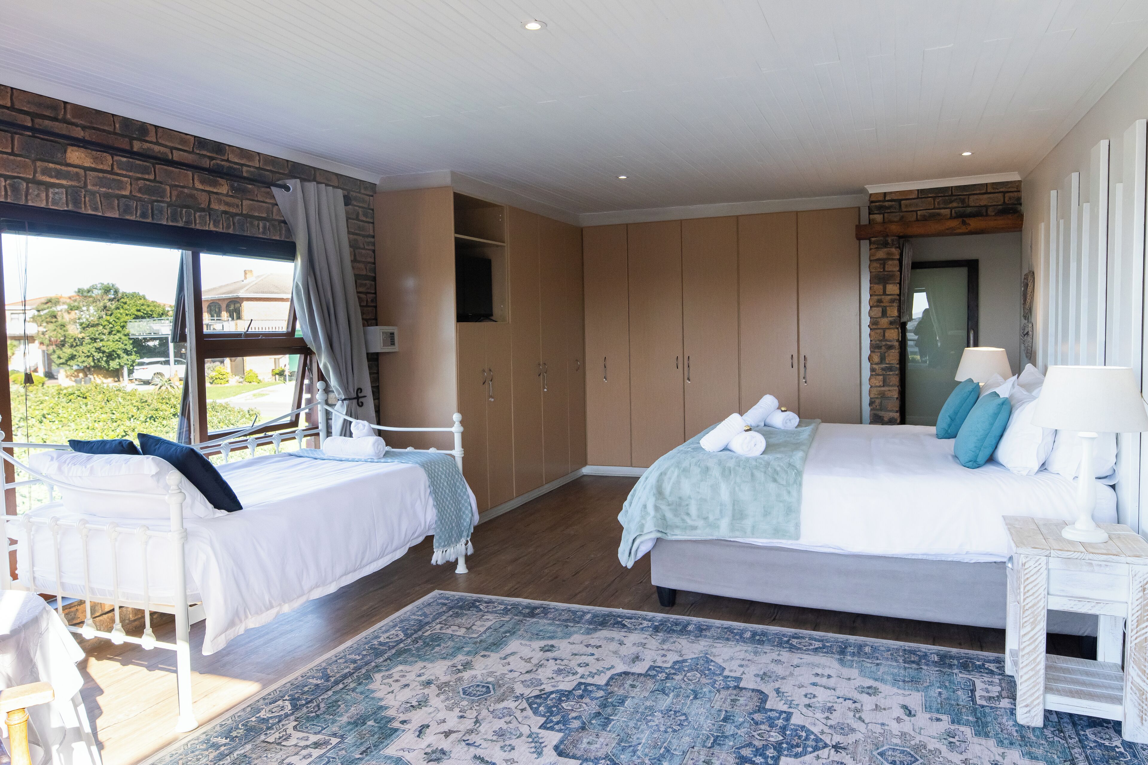 A bedroom with two beds, a large window, and a view of the outdoors.