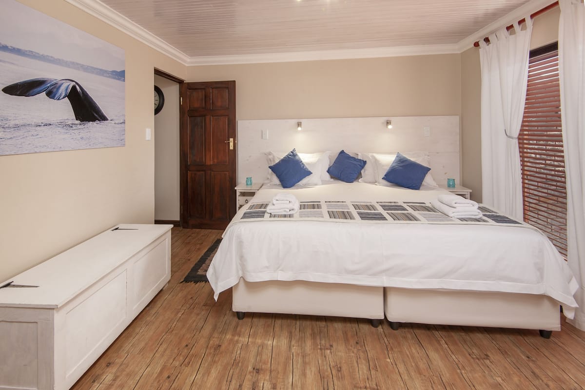 A bedroom with a large bed, a wooden floor, a white headboard, and a wall-mounted clock.
