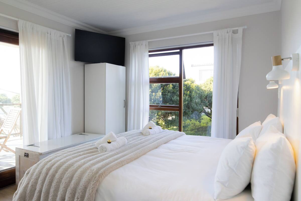 A modern hotel room with a large bed, a flat-screen TV mounted on the wall, and a balcony with a chair.