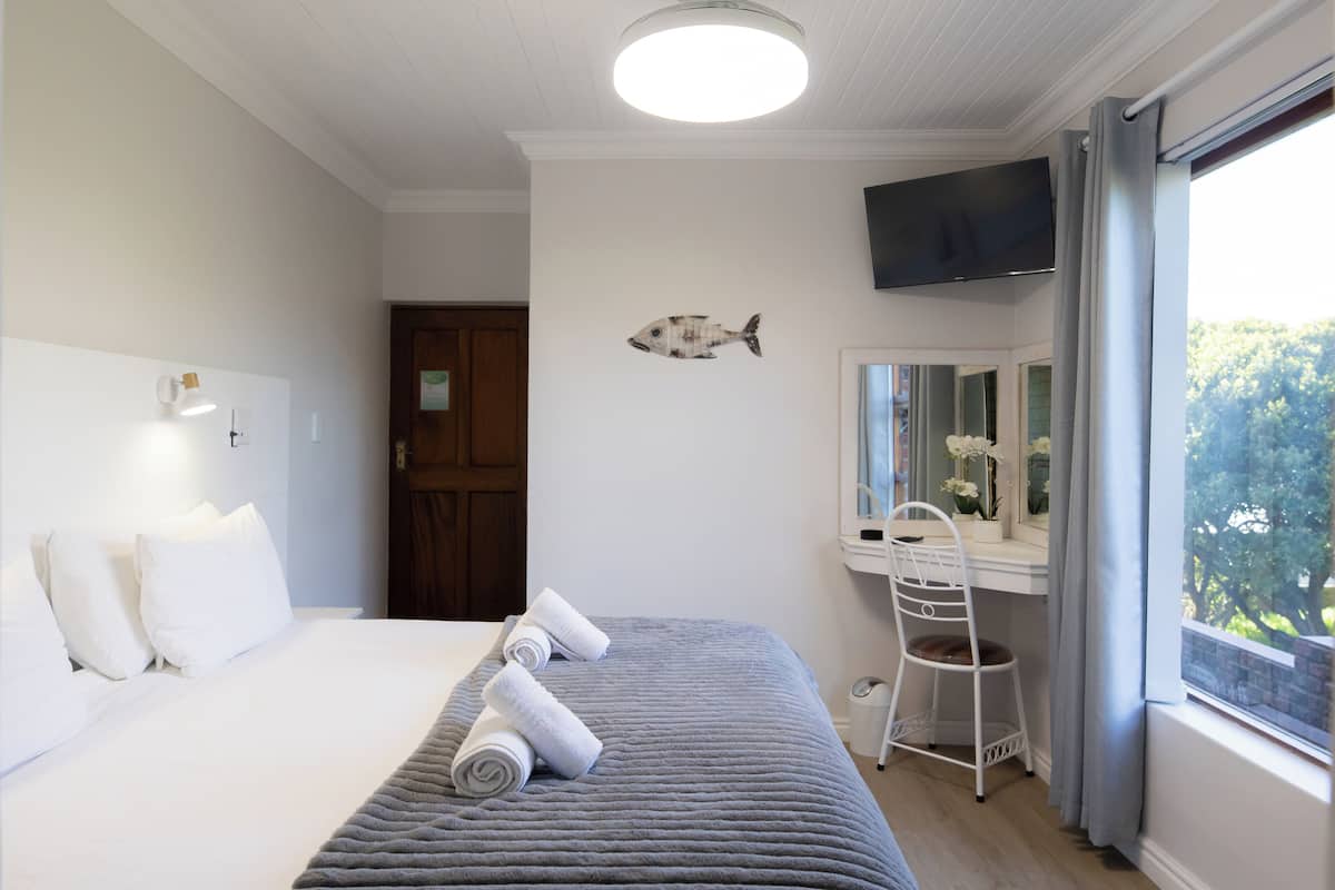 A hotel room with a bed, a desk with a chair, a television, and a fish decoration on the wall.