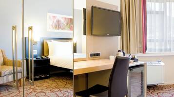 Habitación de hotel con cama, escritorio, silla, televisor y un espejo grande.