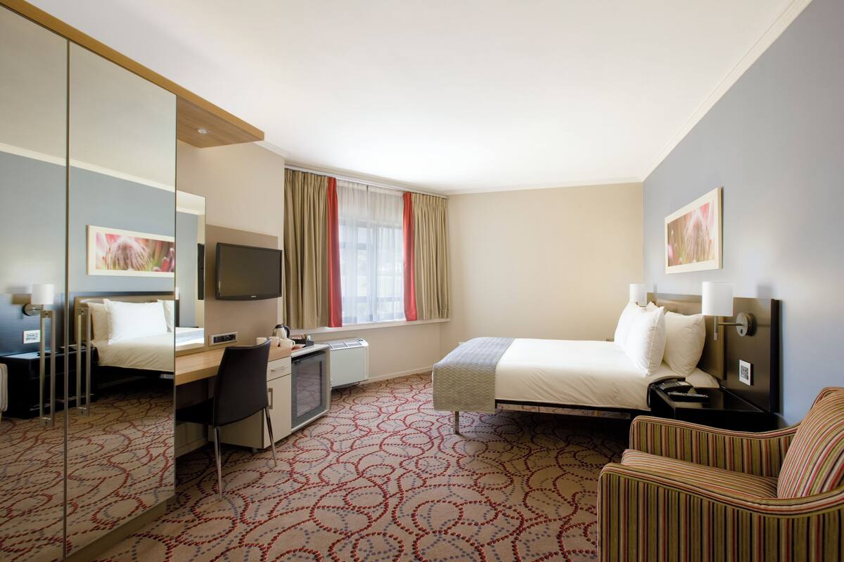 A hotel room with a bed, a desk, a chair, a television, and a large mirror.