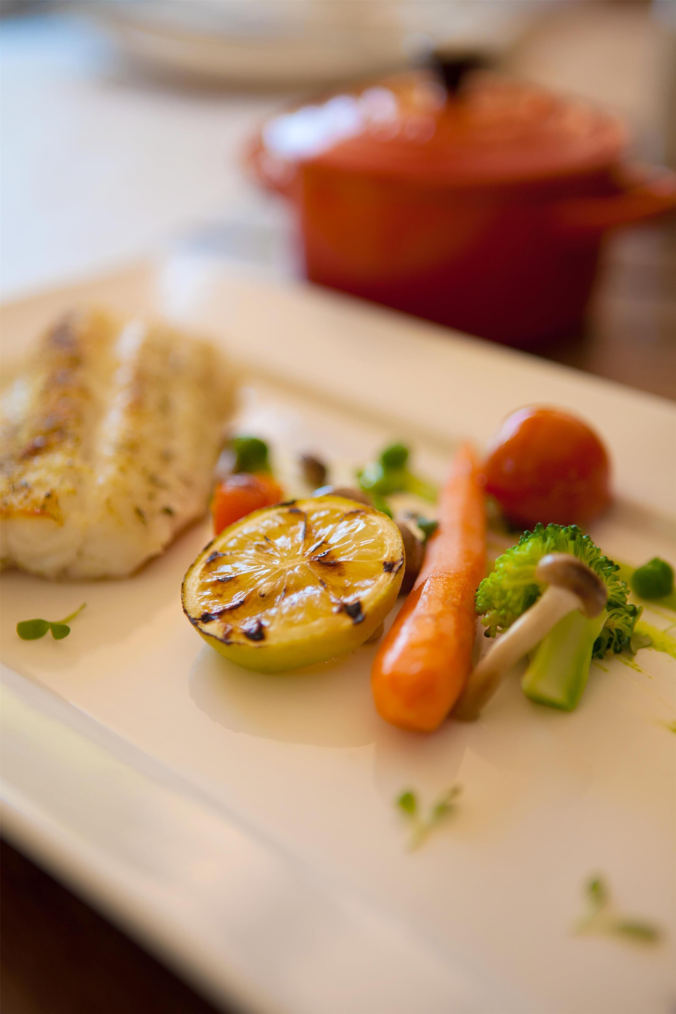 A plate with grilled fish, lemon, broccoli, and carrot.