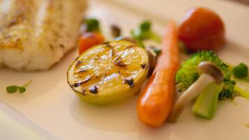 A plate with grilled fish, lemon, broccoli, and carrot.