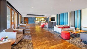 A modern hotel lobby with a long wooden floor, seating areas, a bar, and a TV. - Sunsquare Cape Town Gardens (Cape Town)