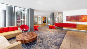 A modern lobby with a sofa, round table, and red chairs. - Sunsquare Cape Town Gardens (Cape Town)