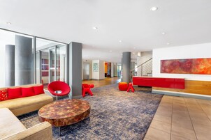 Um hall moderno com sofá, mesa redonda e cadeiras vermelhas.