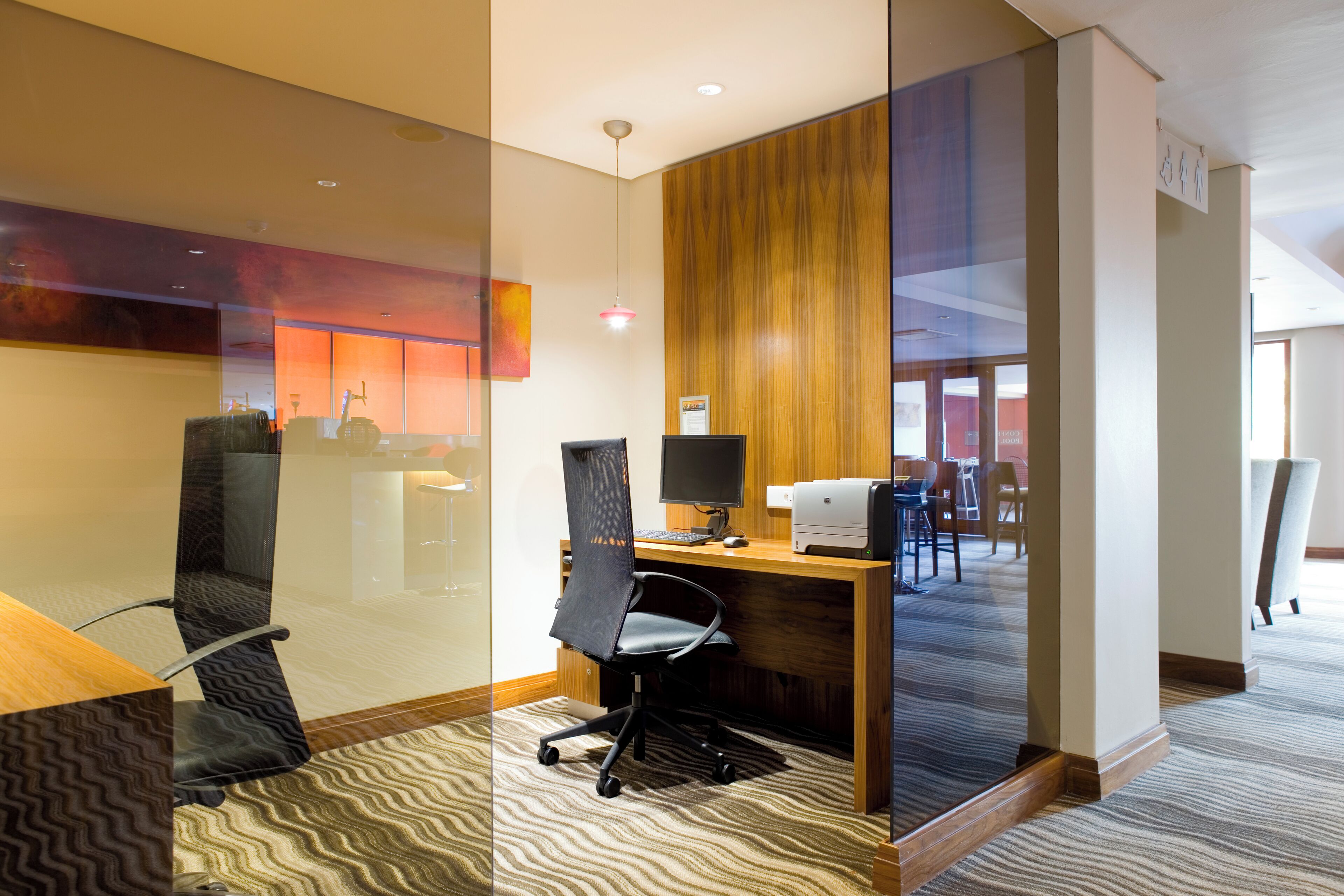 A modern office space with a glass partition, a wooden desk, a computer, and a printer.