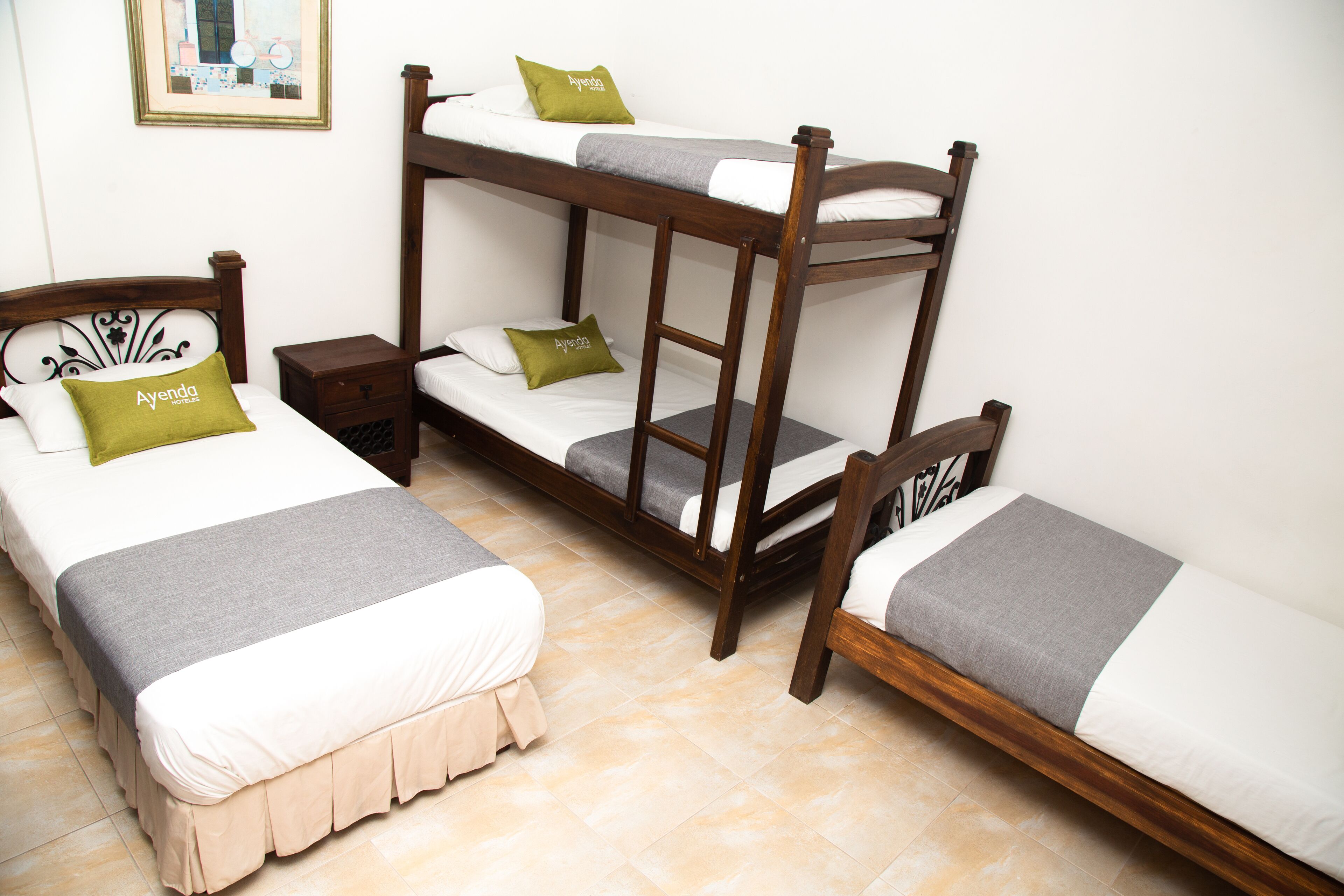 A room with two single beds and a bunk bed, each with pillows and a blanket.
