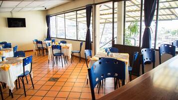 Un restaurante con sillas azules, mesas blancas y ventanas grandes con cortinas.