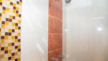 A bathroom with a tiled wall featuring a checkered pattern, a vertical brown tile accent, and a shower with a handheld showerhead.