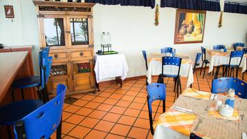 Een restaurant met blauwe stoelen, tafels met witte tafelkleden, een houten kast en een betegelde vloer.