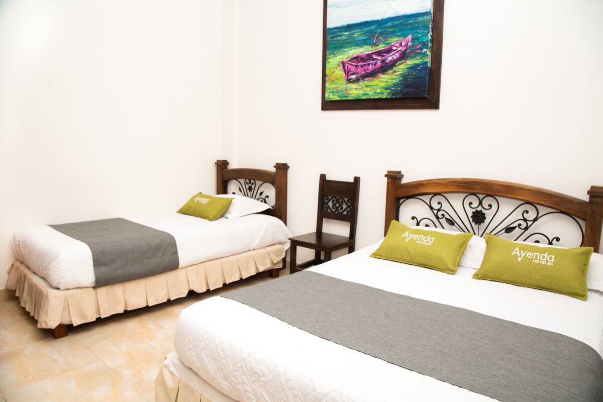 Une chambre d’hôtel avec deux lits, chacun doté d’une tête de lit en bois, une peinture représentant un bateau accrochée au mur et une petite table placée entre les lits.