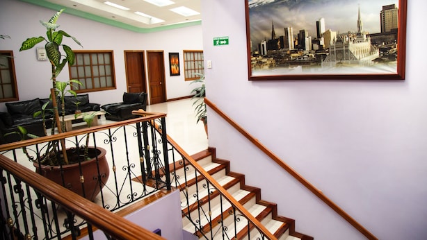 Un hall d’hôtel avec un escalier, un grand tableau représentant un paysage urbain encadré et une plante en pot.